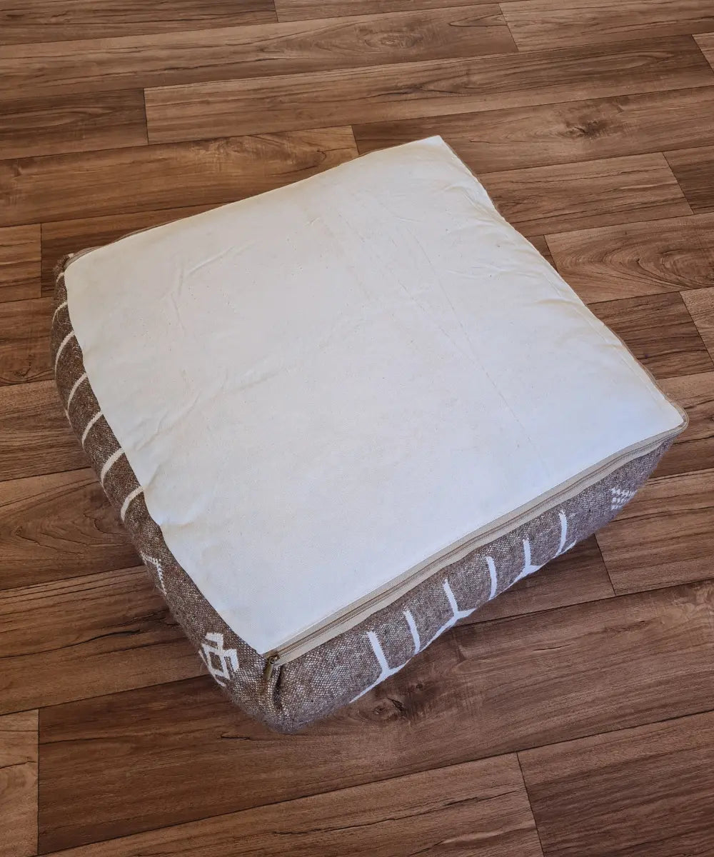 The bottom of the square pouf, showing a simple, off-white cotton canvas back with a large zipper for stuffing