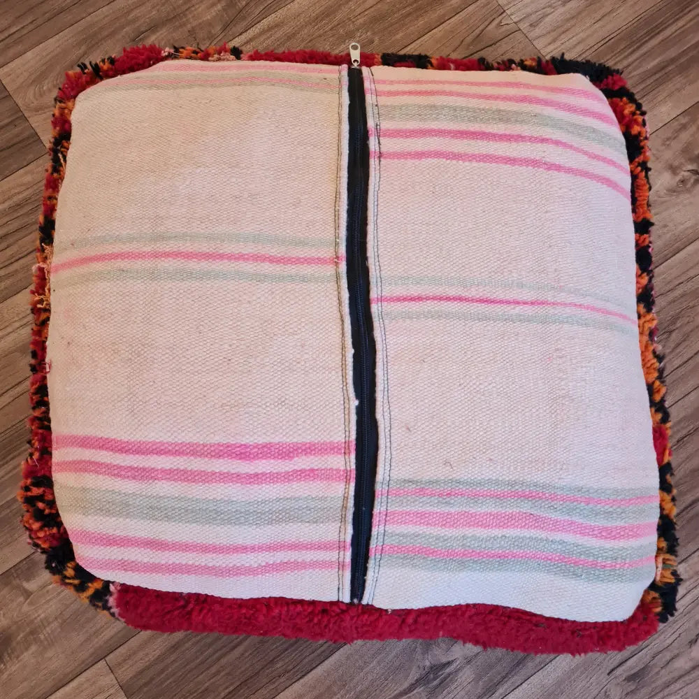 The bottom of the square pouf, showing a flat-woven striped Kilim fabric in shades of cream, pink, and grey, with a large black zipper for stuffing