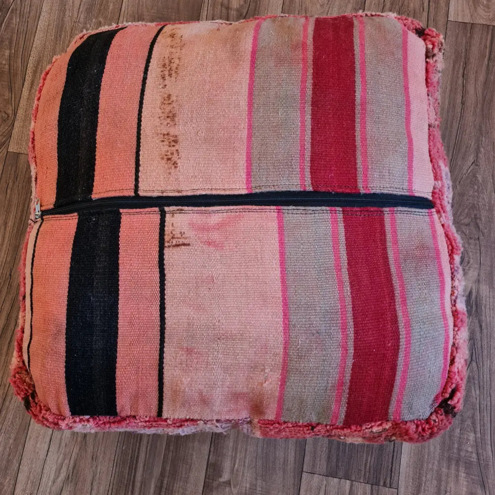 The bottom of the square pouf, showing a flat-woven striped Kilim fabric in shades of red, pink, and black, with a large zipper for stuffing