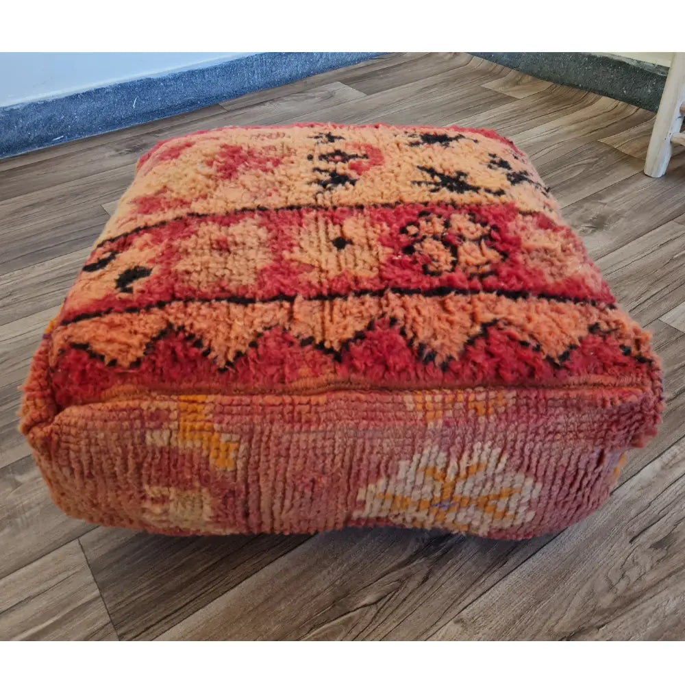 The side profile of a square vintage rug pouf, showing the thick, plush wool texture and colorful patterns