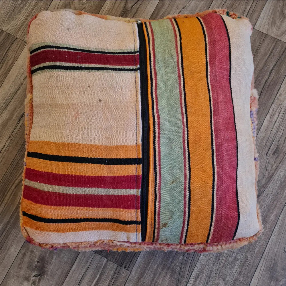 The bottom of the square pouf, showing a flat-woven striped Kilim fabric in shades of red, orange, green, and cream, with a large black zipper for stuffing