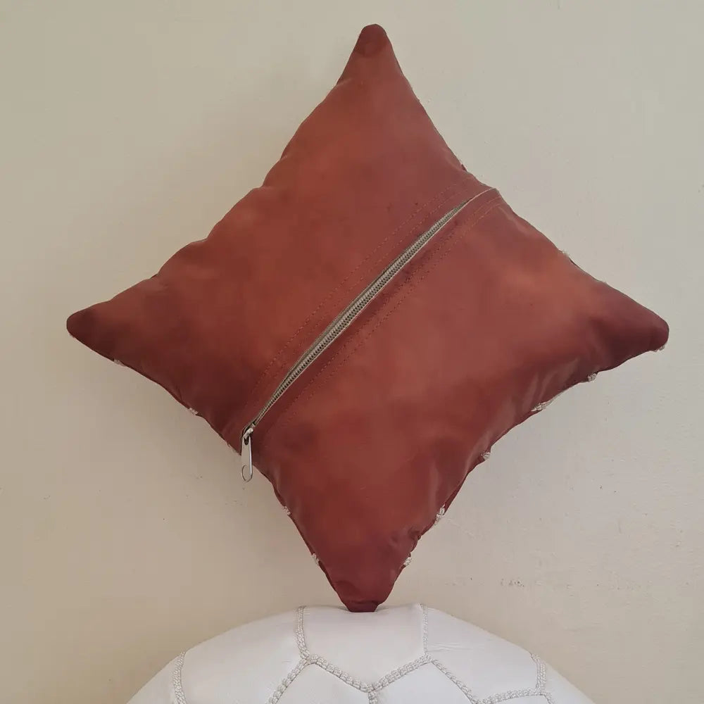 The back of a square tan brown leather pillow cover, showing the long zipper used for inserting a pillow form