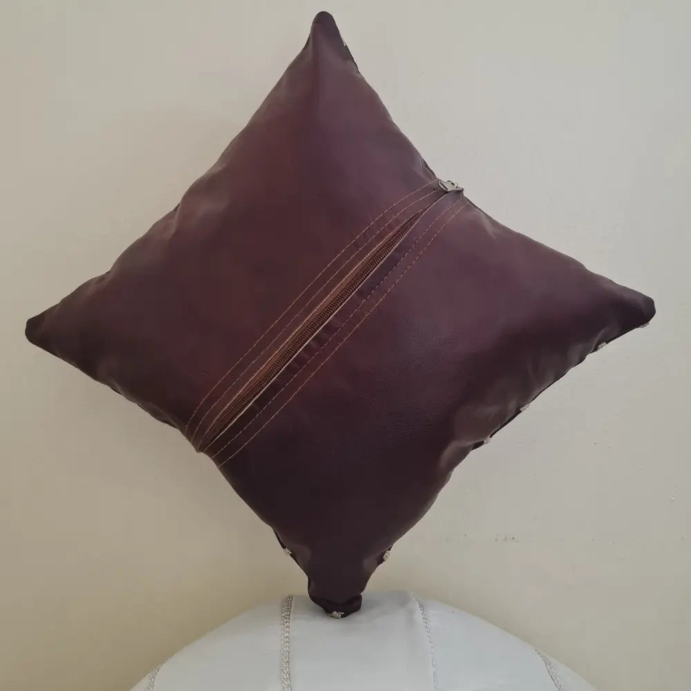 The back of a square brown leather pillow cover, showing the long zipper used for inserting a pillow form