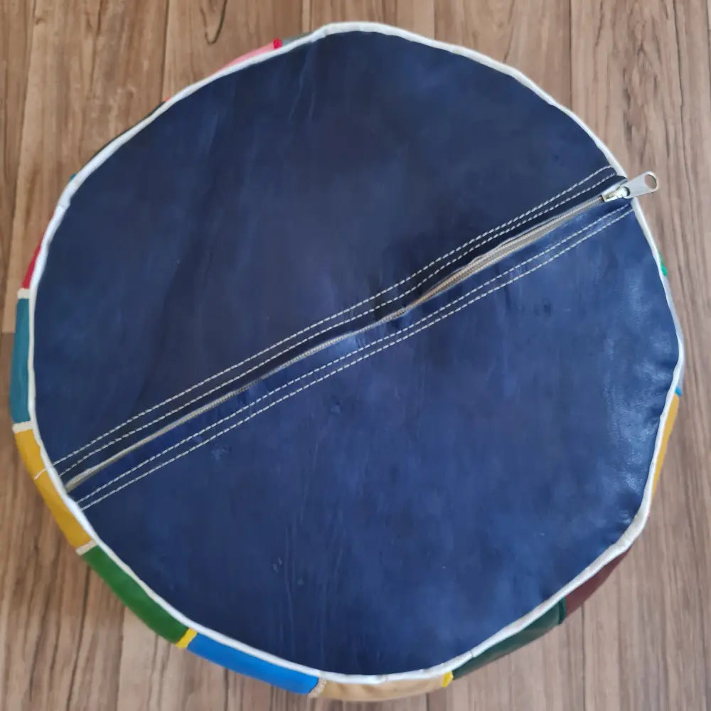 The underside of a patchwork leather pouf, showing a solid dark blue base and the large zipper used for stuffing