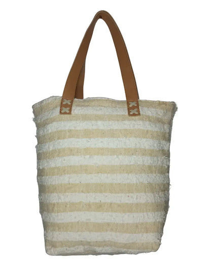 A front-view of a handmade boho-glam tote bag. The bag's body is made of textured cream eyelash fringe and is decorated with a grid of shimmering gold sequins. It features two tan-brown leather shoulder straps, and its dimensions are displayed on the image.
