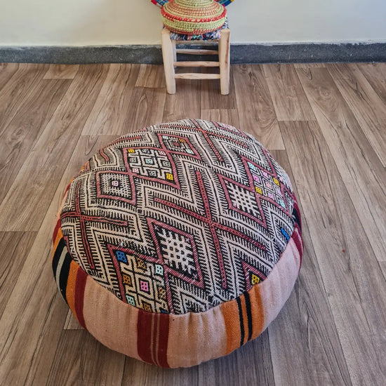 A detailed close-up shot of the intricate woven texture of a vintage Kilim rug, showing the geometric patterns in black, red, and beige with small colorful accents.
