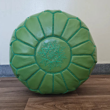 A top-down view of a handmade, round Moroccan pouf in vibrant green leather. It features geometric, hand-stitched seams and a central embroidered star design in matching green thread