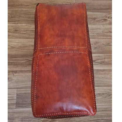 A front view of a large, handmade rectangular Moroccan pouf in a rich, distressed brown leather. It features thick, contrasting off-white hand-stitching