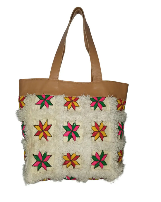 Front view of a handmade tote bag. The bottom is cream-colored fuzzy patchwork with colorful embroidered stars. The top and handles are tan leather. Dimensions are annotated.

