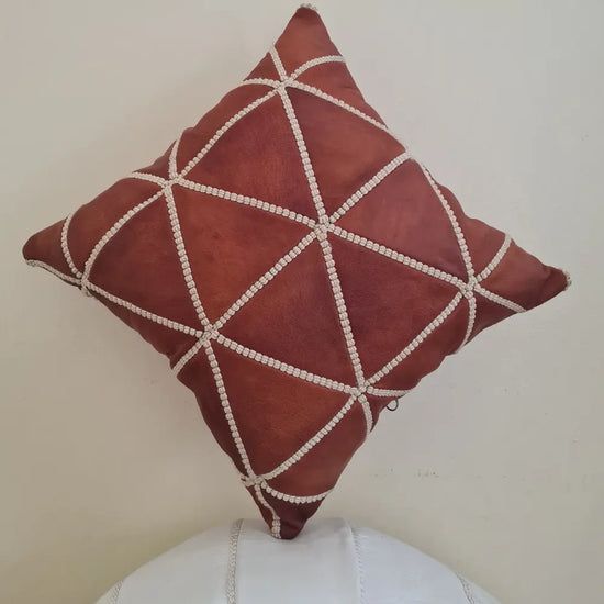 A handmade, square Moroccan throw pillow cover in rich, tan brown leather. It features a geometric diamond pattern created with thick, off-white hand-stitching
