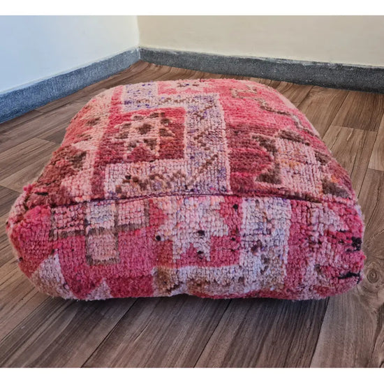 The side profile of a square vintage rug pouf, showing the thick, plush wool texture and the faded, multi-toned pink and red colors