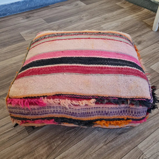 The side profile of a square vintage Kilim pouf, showing the durable woven texture and the textured fringe along the colorful striped pattern