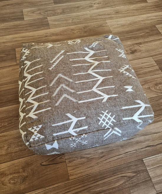 The side profile of a square modern pouf, showing the durable woven texture and the continuation of the white tribal patterns on the brown background