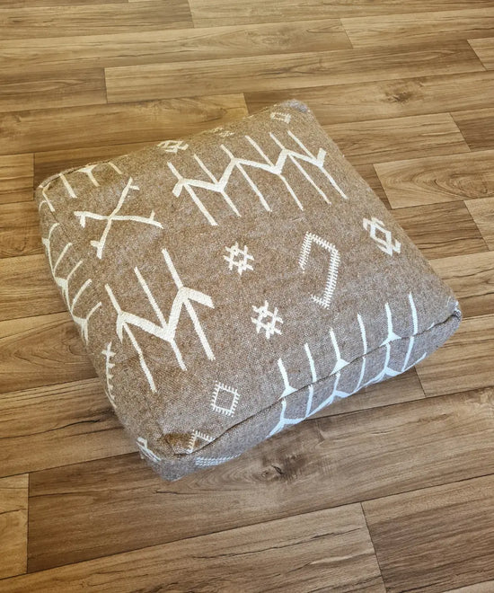The side profile of a square modern pouf, showing the durable woven texture and the continuation of the white tribal patterns on the brown background