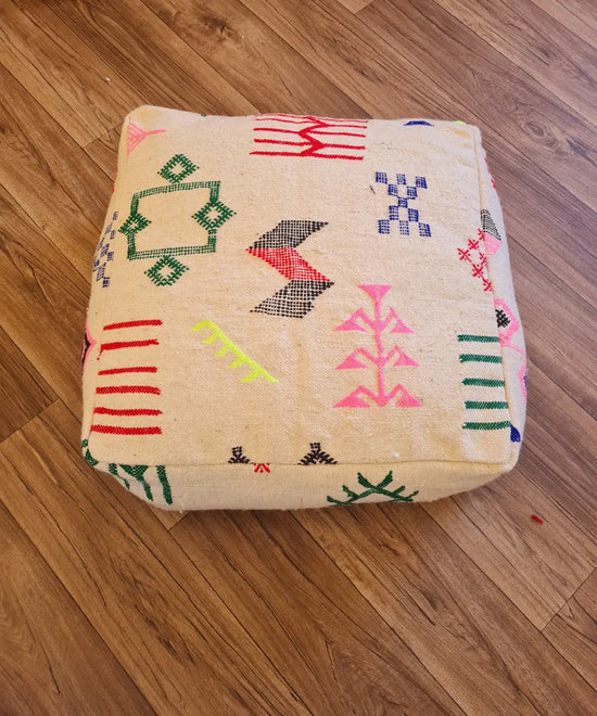 The side profile of a square modern Kilim pouf, showing the durable woven texture and the vibrant, colorful embroidery along the side