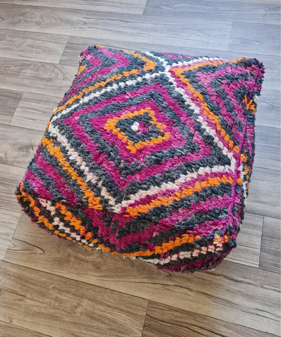 The side profile of a square vintage rug pouf, showing the thick, plush shag texture and the rich, multi-toned color palette of magenta, orange, and charcoal