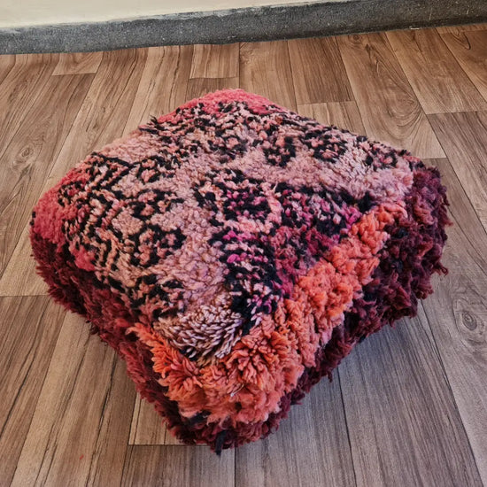 The side profile of a square vintage rug pouf, showing the thick, plush wool shag and the rich, multi-toned color palette
