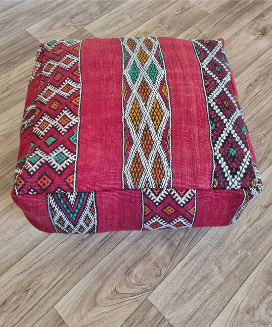 The side profile of a square vintage Kilim pouf, showing the durable woven texture and the continuation of the colorful geometric patterns in red and green