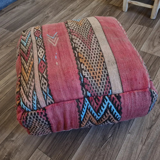 The side profile of a square vintage Kilim pouf, showing the durable woven texture and the beautifully faded, multi-toned red and pink colors