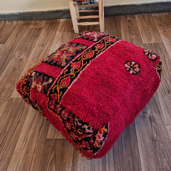 The side profile of a square vintage rug pouf, showing the thick, plush wool shag and the rich red color.
