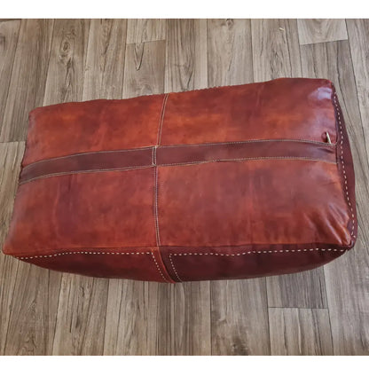 The underside of a rectangular brown leather pouf, showing the large zipper used for stuffing