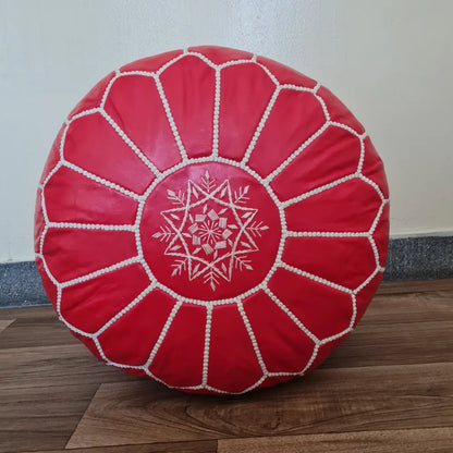The underside of a red leather pouf, showing the large zipper used for stuffing, set against a dark wood floor